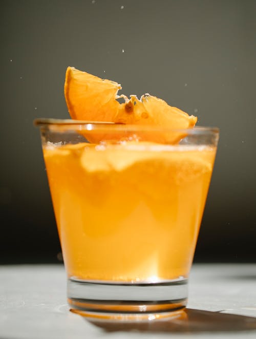 Glass of fresh cold beverage decorated with piece of orange on thin wooden stick