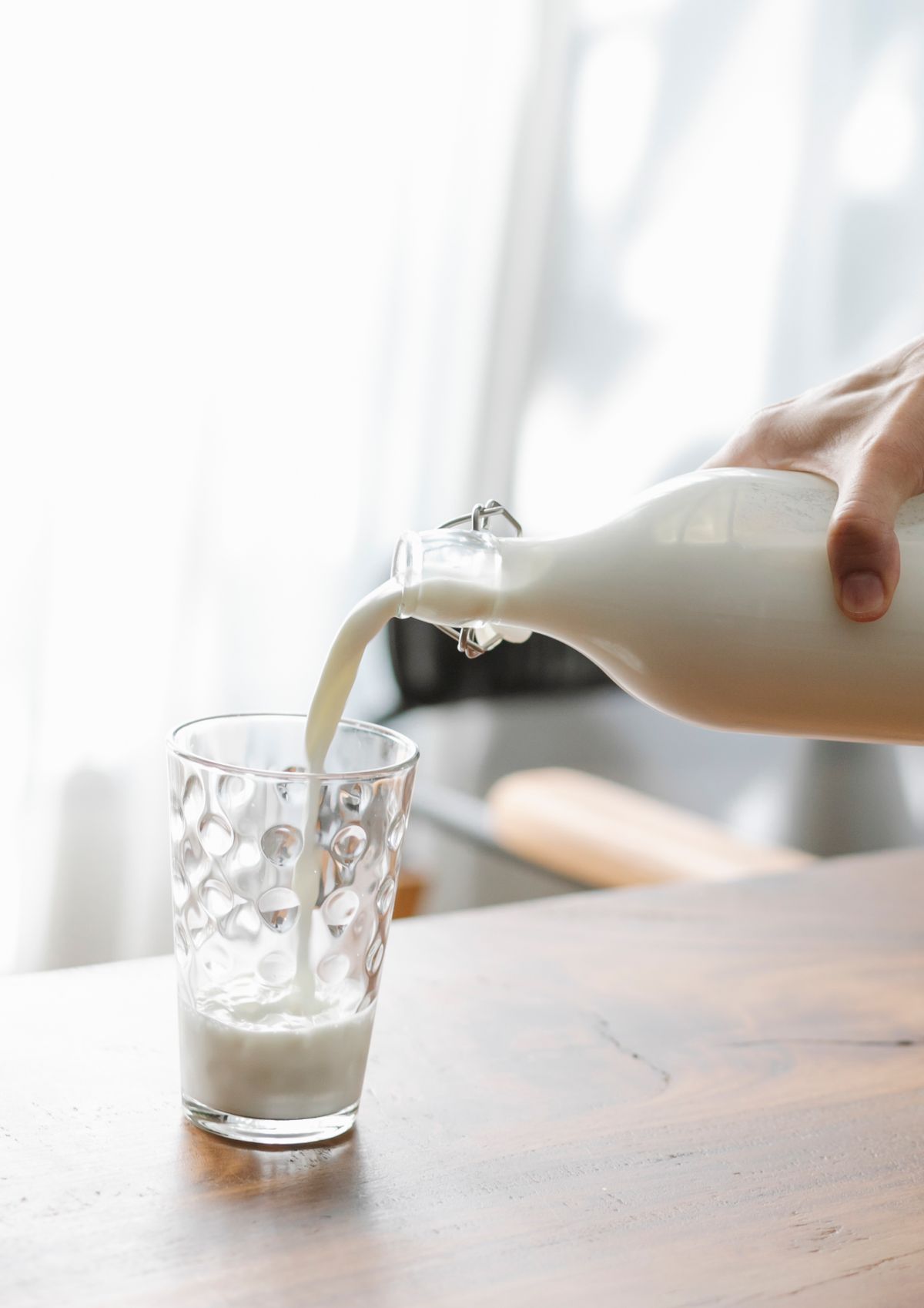 Person pouring fresh milk into a glass on a wooden table, illustrating lactose as one of the foods that cause bloating