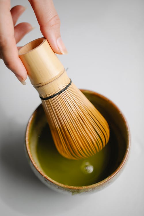 Crop woman with matcha tea and whisk