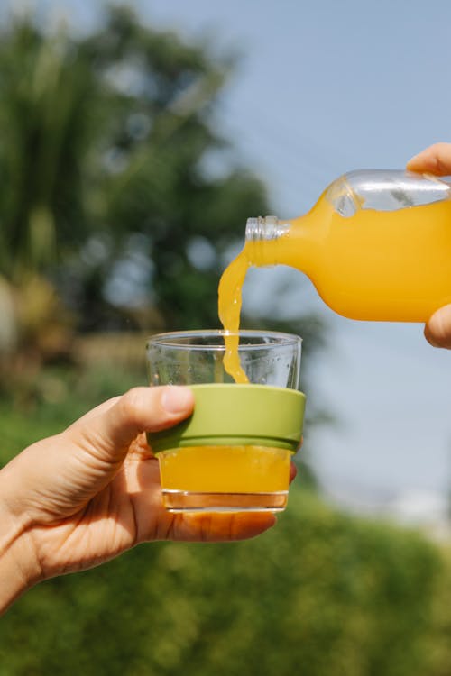 Free Crop unrecognizable person pouring fresh orange juice from bottle into glass on blurred background Stock Photo