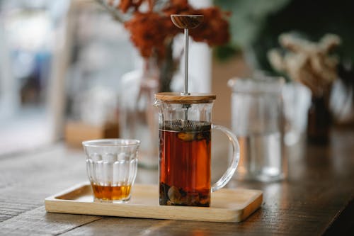 Free Transparent French press with hot aromatic herbal tea brewing on wooden tray near glass on table in cafe Stock Photo