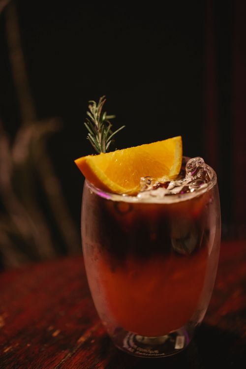 Free Crystal clean glass of alcoholic drink with ice cubes and decorated with slice of orange and rosemary on table in bar Stock Photo