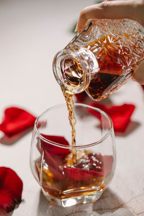 Free Crop person pouring alcohol into glass with petals Stock Photo