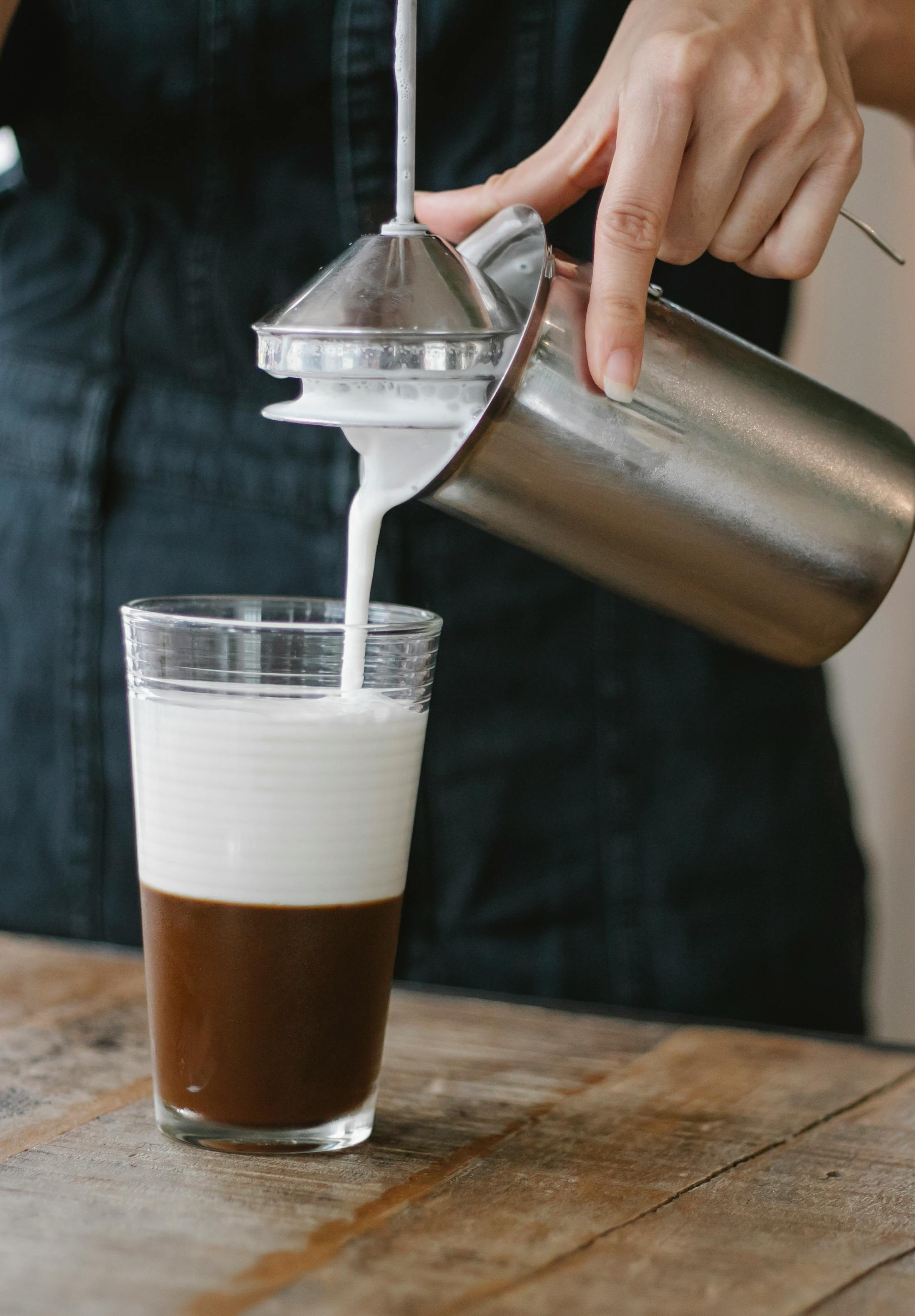 crop barista pouring milk in glass with coffee