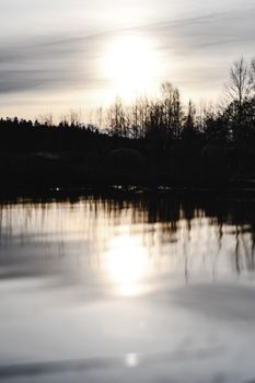 芬兰赫尔辛基的一个湖面上，倒映着宁静的日落景象，湖岸树木的剪影清晰可见
