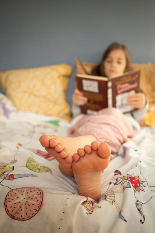 Free A Girl Lying on the Bed while Reading a Book Stock Photo