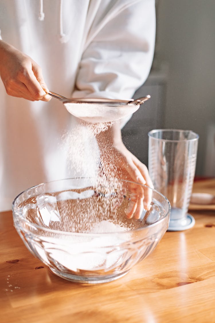 A Person Sifting Powder Into A Bowl