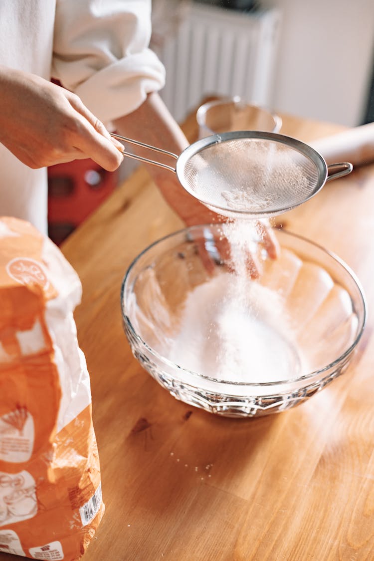 A Person Sifting Powder Into A Bowl