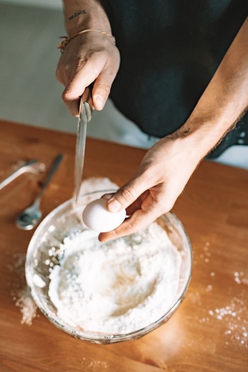 Free A person cracks an egg into a bowl of flour, preparing to bake. Stock Photo