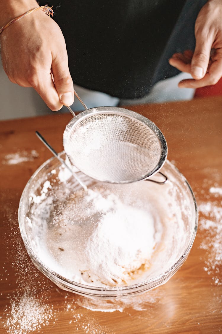 A Person Sifting Powder Into A Bowl