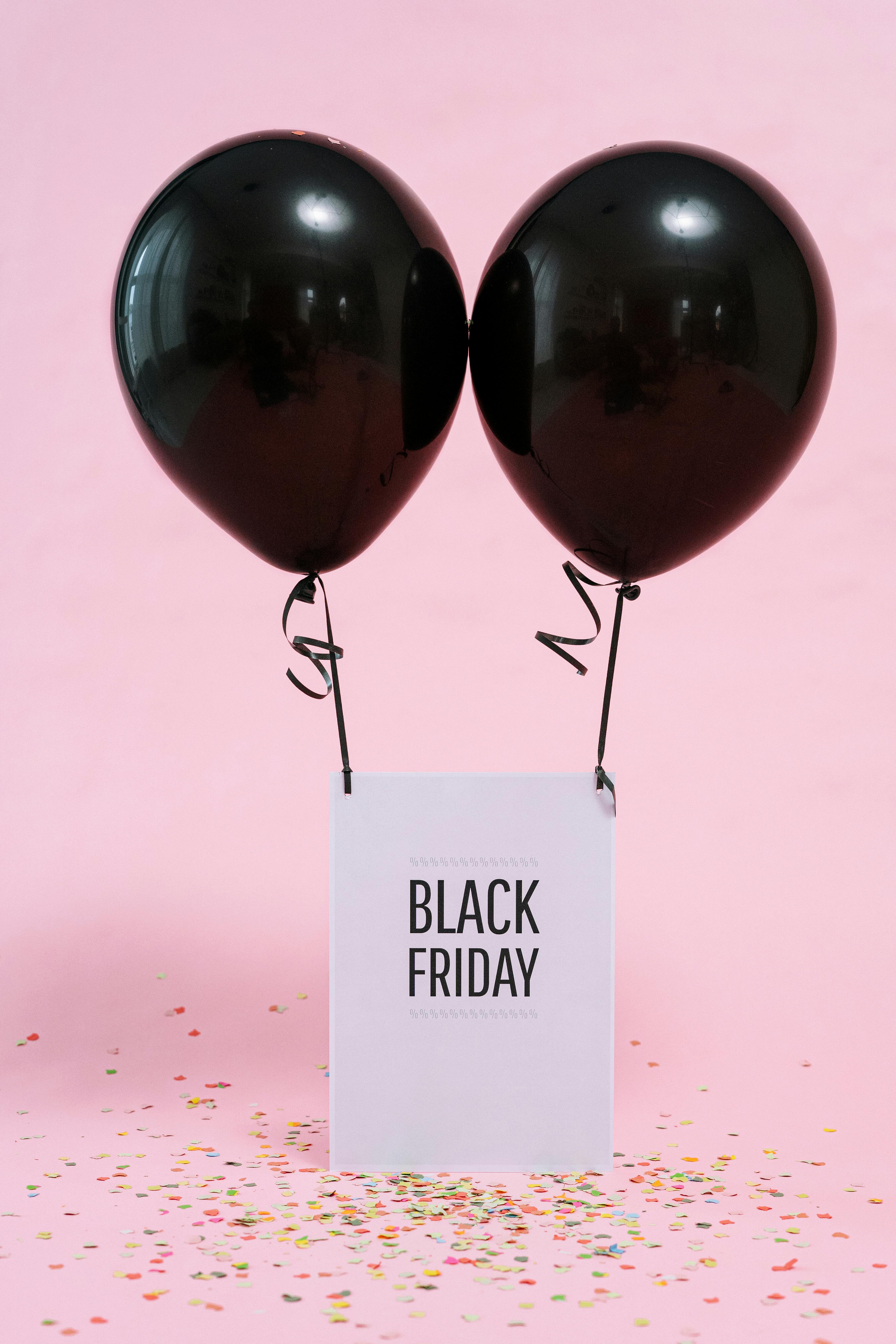 Black balloons with Black Friday tag and scattered confetti on a pink background. Perfect for sales and marketing visuals.