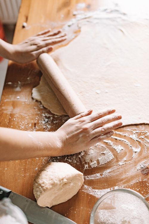 Free Person kneading and rolling dough with flour on a wooden kitchen table. Stock Photo