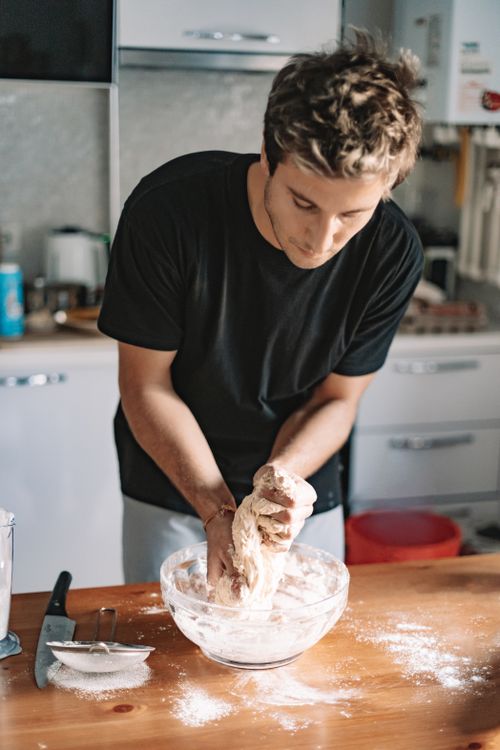 Free A young man kneads dough in a glass bowl in a modern kitchen setting, creating a homemade, rustic vibe. Stock Photo