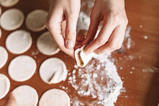 Hands preparing homemade dumplings with dough and flour on a wooden surface.