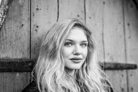 Black and white portrait of a woman with long hair and a lip piercing against a wooden background.