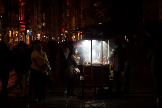 Bustling night street with illuminated food cart and people gathering.