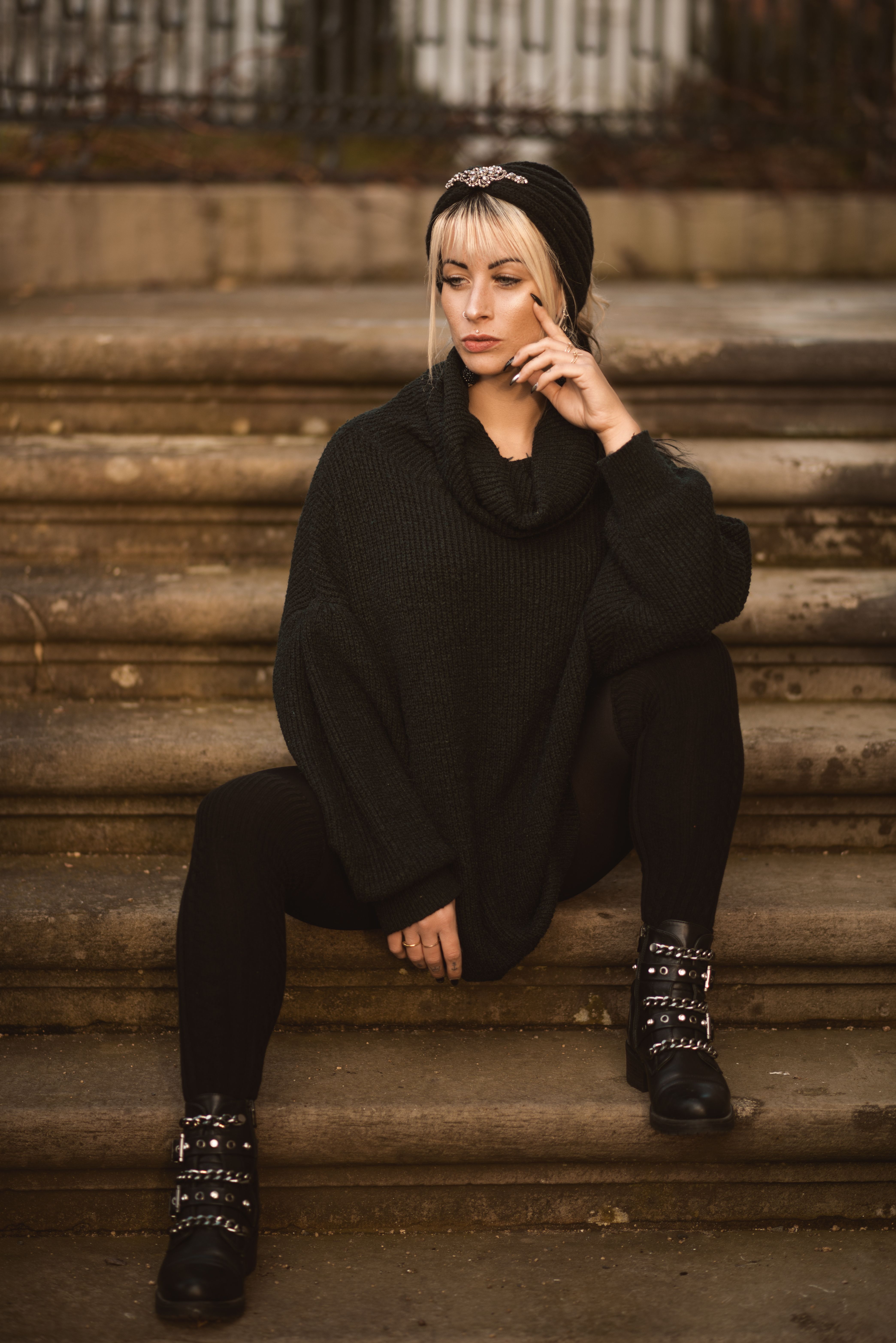 A fashionable woman in a black outfit sitting thoughtfully on concrete stairs.