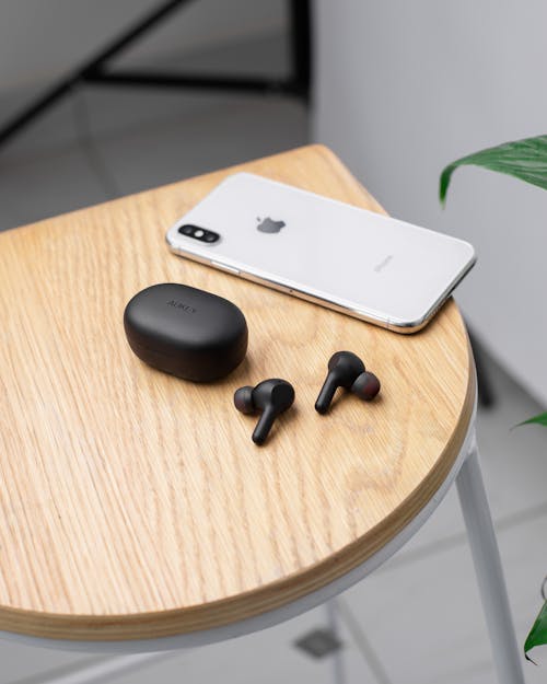 Free Close-Up Shot of an Iphone beside a Pair of Earbuds on a Wooden Table Stock Photo