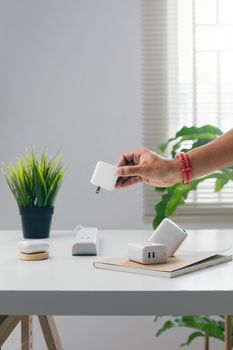 Close-up of a hand holding a white adapter in a modern workspace with plants and natural light.