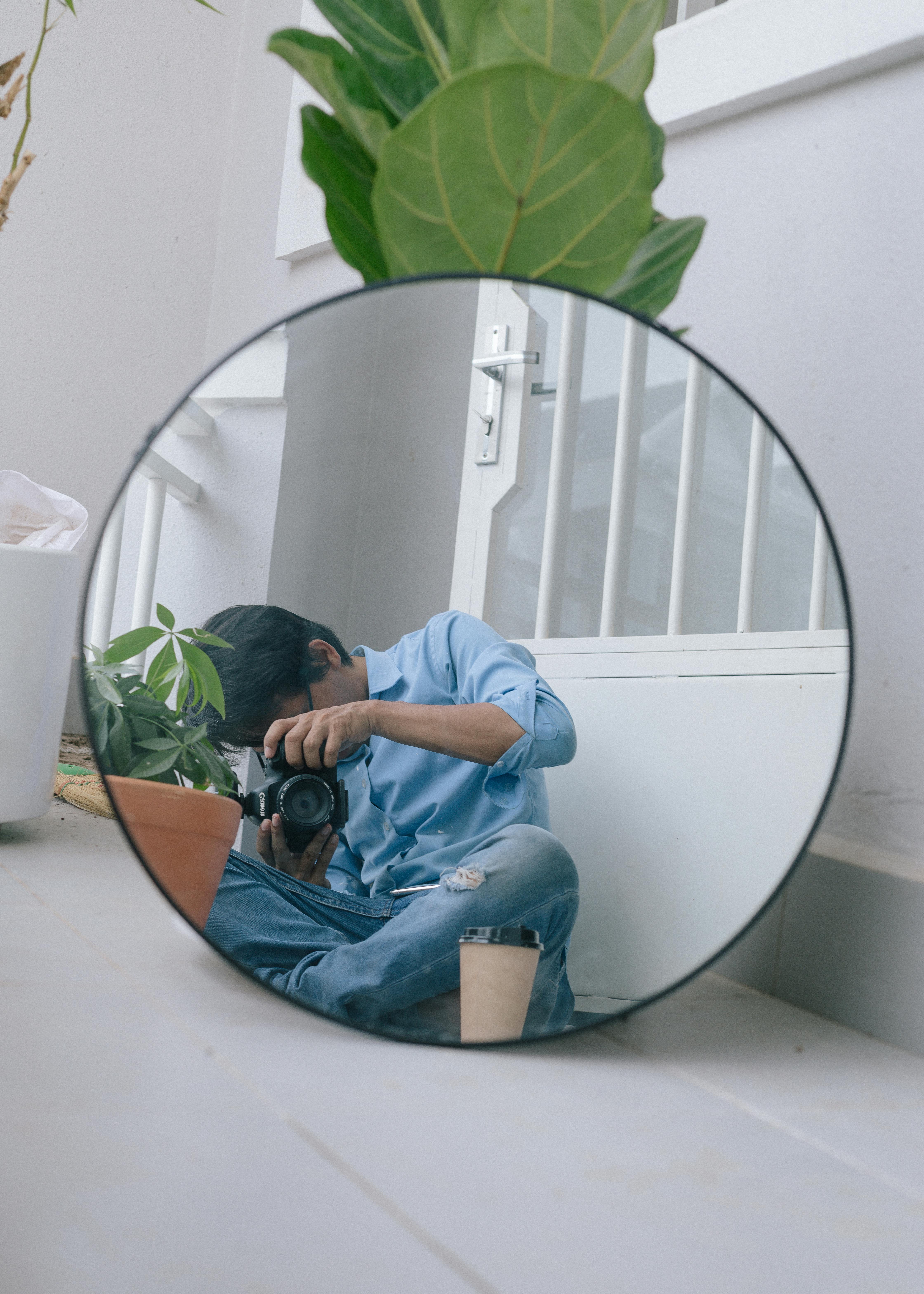 Reflection of a photographer capturing a self-portrait with a DSLR through a round mirror.