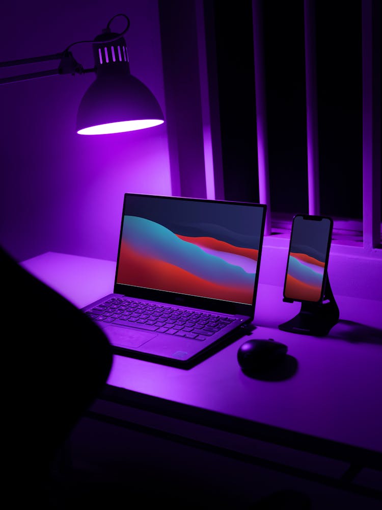 Laptop And A Smartphone On A Desk With A Purple Light Lamp 