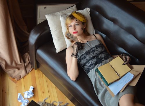 Free From above of young pondering female writer in old fashioned dress lying on couch with empty notepad and looking up Stock Photo