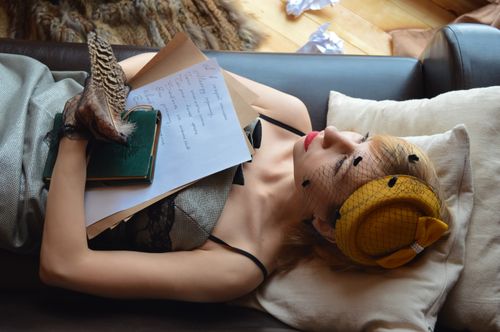 Free High angle of young dreamy female author in retro apparel with book and feather looking up on sofa at home Stock Photo