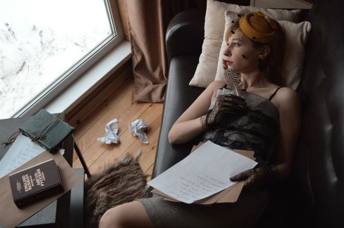 Free High angle of young wistful female author in vintage wear with feather looking away on couch against window Stock Photo