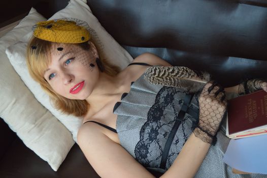 From above of young dreamy female author in old fashioned outfit with textbook and feather looking away on sofa