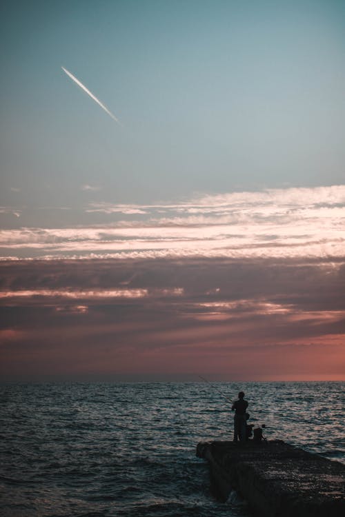 Free Silhouette of a Person Fishing at Sunset Stock Photo