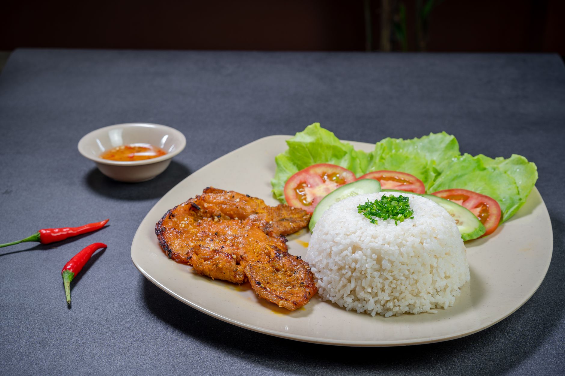 Delicious grilled pork served with rice, lettuce, tomatoes, and cucumber on a plate.