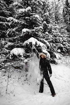 Man enjoying nature in snow-covered Helsinki forest, shaking a spruce tree branch.