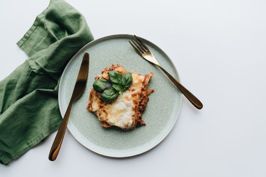 A flatlay of traditional Italian lasagna garnished with fresh basil, styled with elegant cutlery.