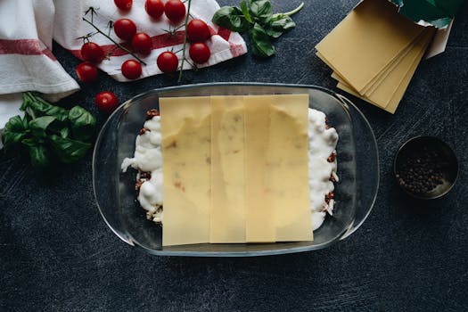 Flat lay of lasagna preparation with fresh ingredients and pasta sheets.