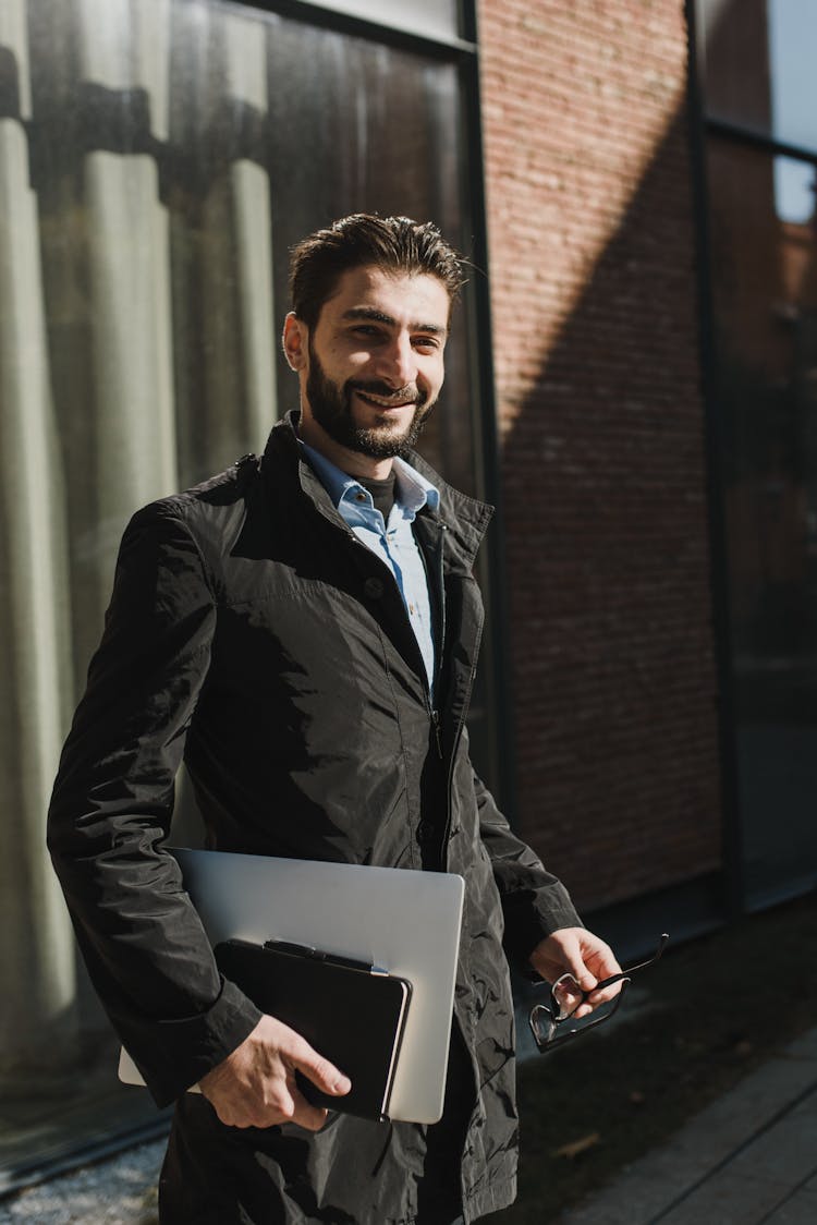 Smiling Man In Black Jacket Holding A Laptop