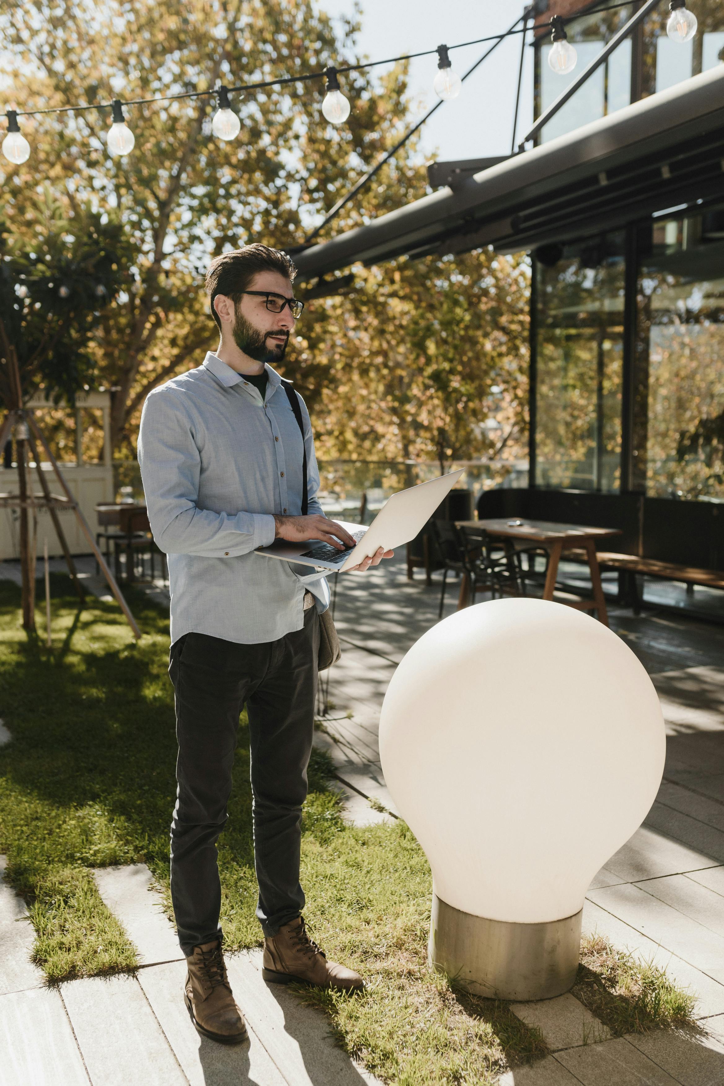 年轻人站在装饰灯泡旁使用笔记本电脑