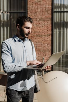 Bearded man in blue shirt using laptop outdoors, remote work concept.
