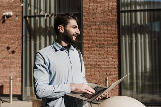 Cheerful businessman working outside with a laptop on a sunny day.