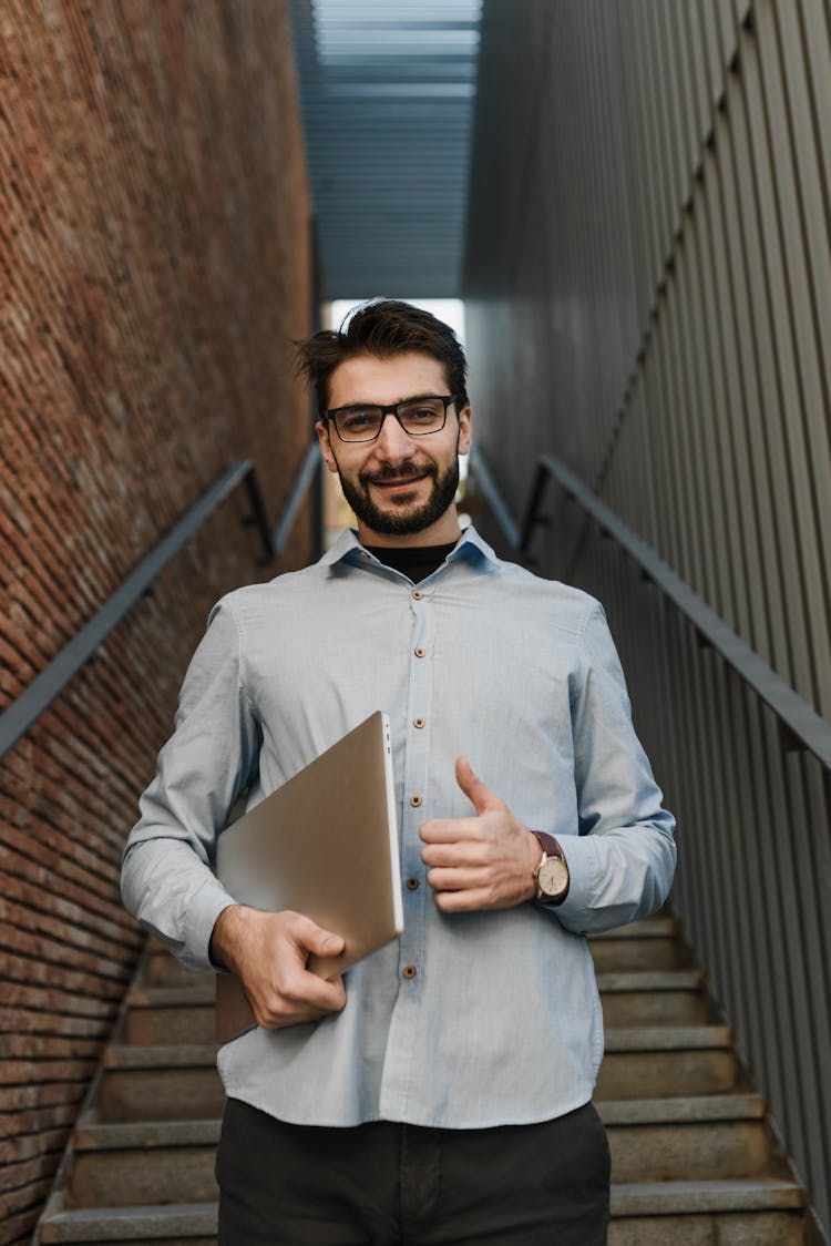 A Man Carrying A Laptop Doing A Thumb Up Gesture