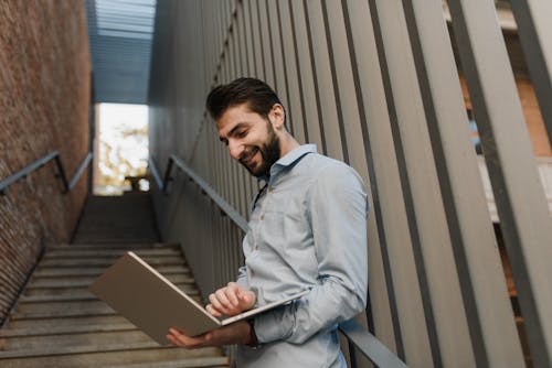 A Smiling Man Using His Laptop while Leaning on a Handrail