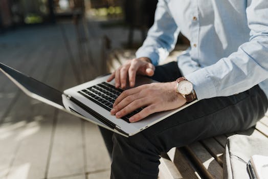 Person typing on a laptop outdoors, showcasing remote work setup with casual attire.