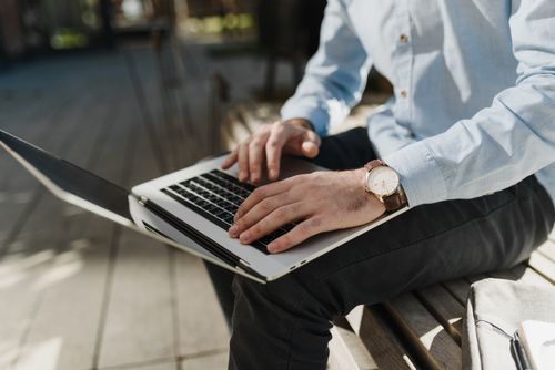 Free Person typing on a laptop outdoors, showcasing remote work setup with casual attire. Stock Photo