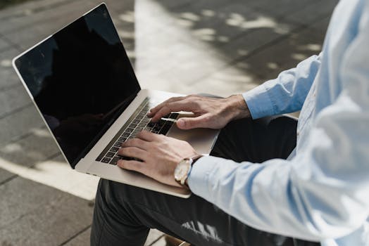 A man uses a laptop outdoors, illustrating remote work concept.
