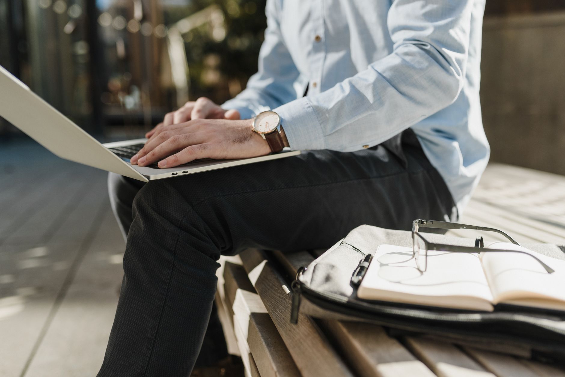 Person working remotely on a laptop outdoors, with a notebook and glasses nearby for productivity.