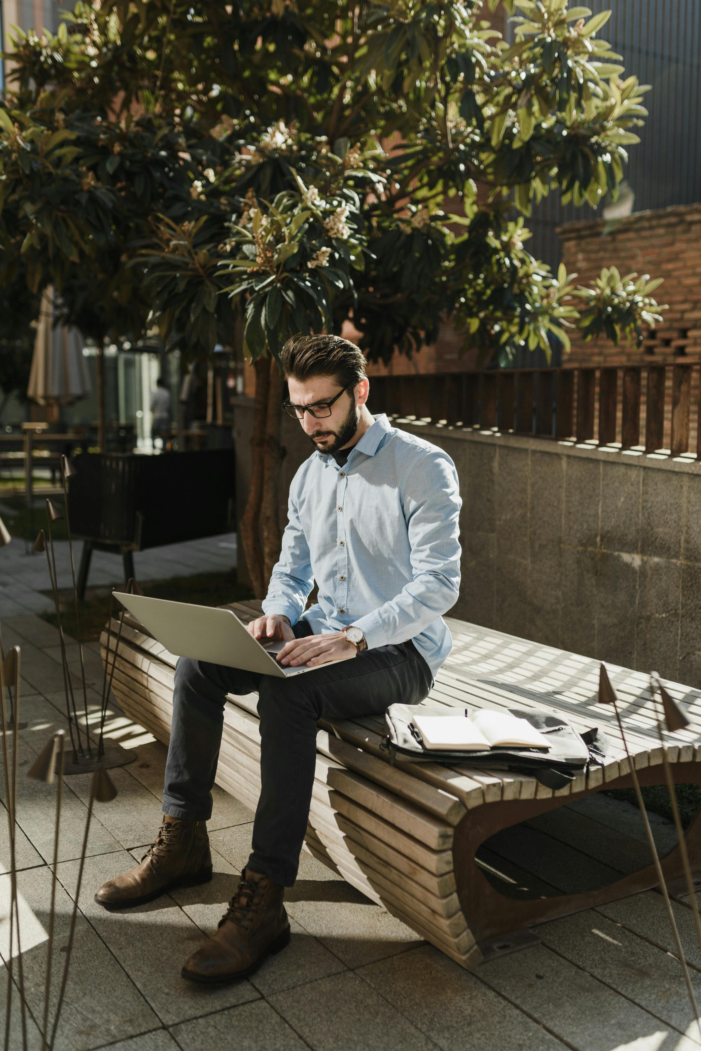 Caucasian man working on laptop outdoors, enjoying remote work environment.
