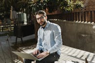 Man in Blue Dress Shirt and Black Pants Sitting on Wooden Bench