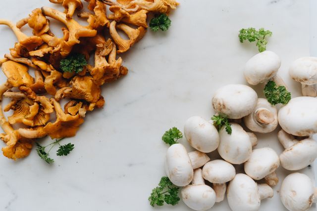 Golden chanterelles and white button mushrooms with parsley sprigs on white marble