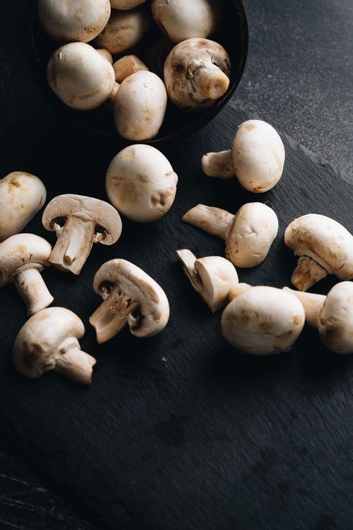 Free A close-up of fresh Agaricus mushrooms on a dark slate surface, perfect for culinary themes. Stock Photo