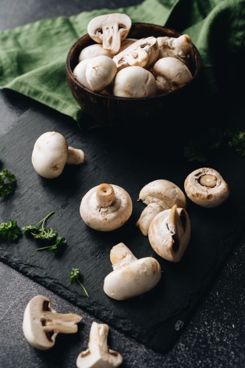 Free Close-up of fresh white mushrooms on dark slate with green herbs, ideal for culinary visuals. Stock Photo