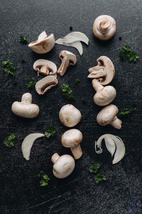 Free Close-up of fresh Agaricus bisporus mushrooms and herbs on a dark background, showcasing culinary ingredients. Stock Photo